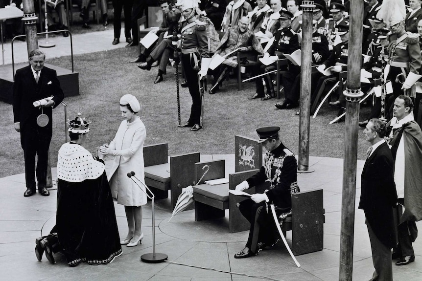 A black and white photograph of Prince Charles kneeling in front of the Queen during his Investiture Ceremony.