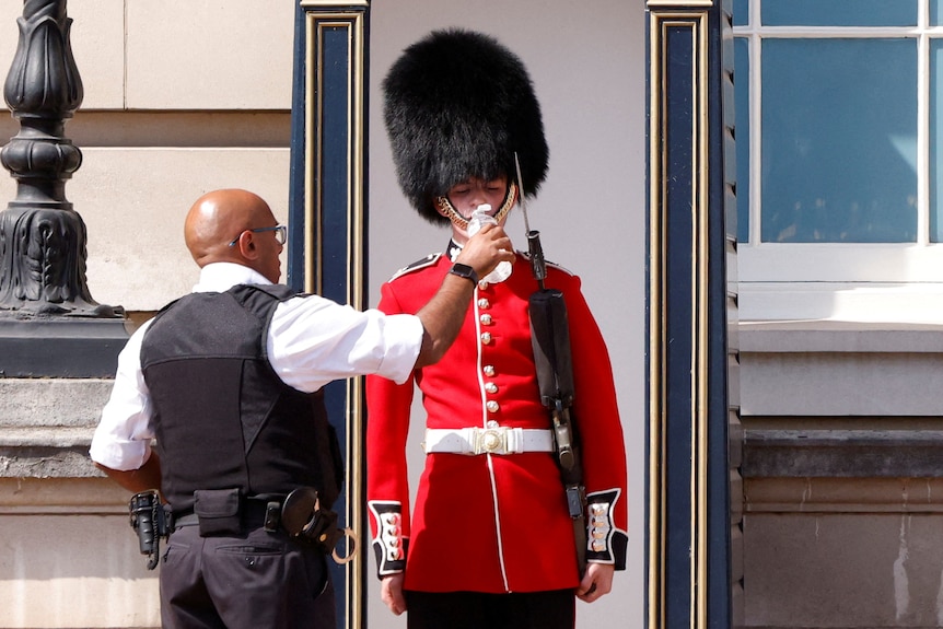 A police officer puts a bottle of water to a Queen's Guard soldier, who is wearing full traditional uniform.