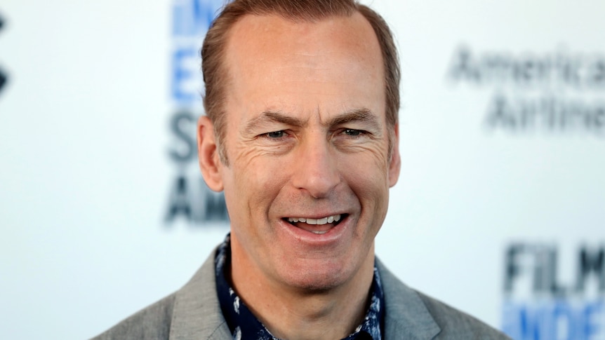 Bob Odenkirk smiles while wearing a light grey suit.