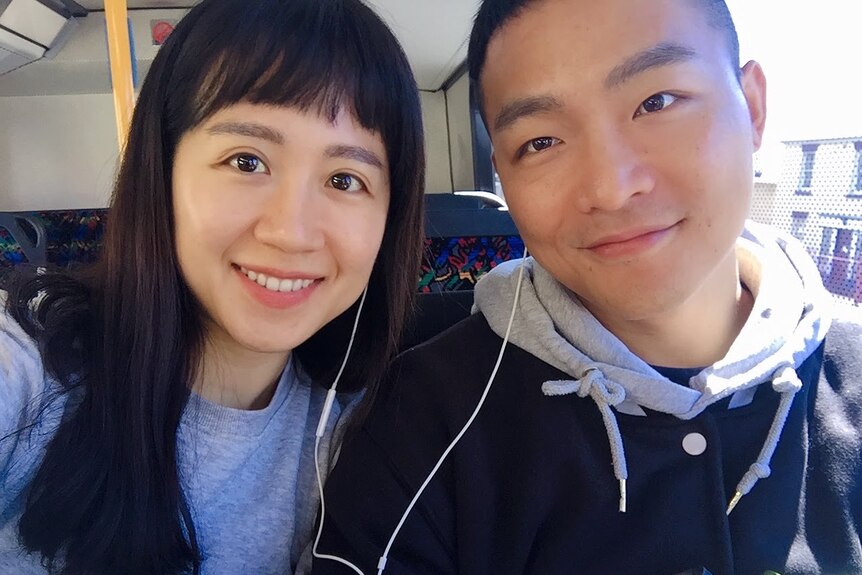 A young Korean couple smiling on a train.
