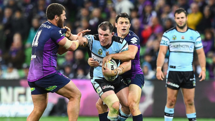 Cronulla's Paul Gallen (C) is tackled by Melbourne's Kenny Bromwich and Cooper Cronk at AAMI Park.