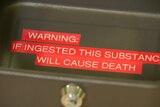 A close-up image of a black metal box with a lock, with red text warning the substance contained in the box will cause death.