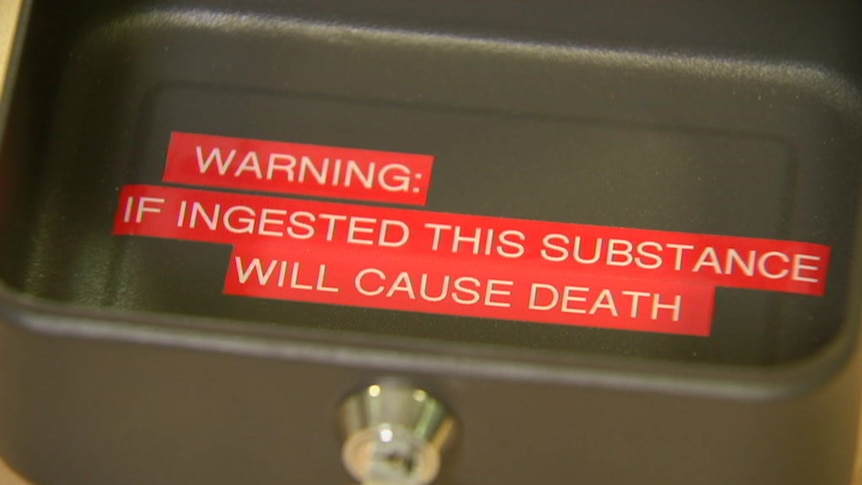 A close-up image of a black metal box with a lock, with red text warning the substance contained in the box will cause death.