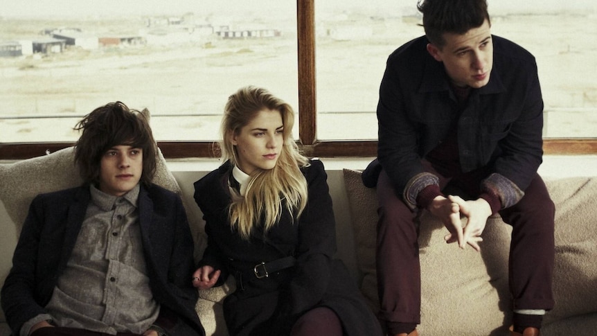 The three members of London Grammar sit looking off camera to the left in what looks like an airport lounge