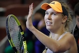 A tennis player raises her hand and racquet in salute to the crowd after winning a match.