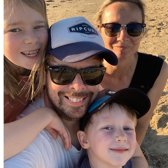 A man in sunglasses with his wife and kids around him on the beach