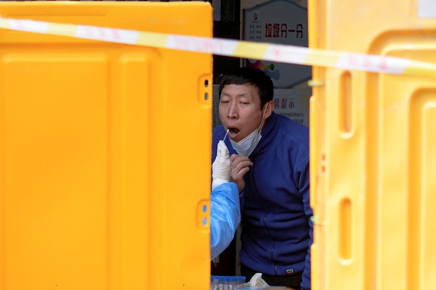A man gets tested for COVID at a makeshift testing facility behind yellow barriers.