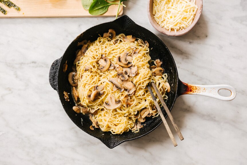 Pan of ramen noodles with mushrooms and cheese being mixed through with chopsticks, a quick weeknight meal.