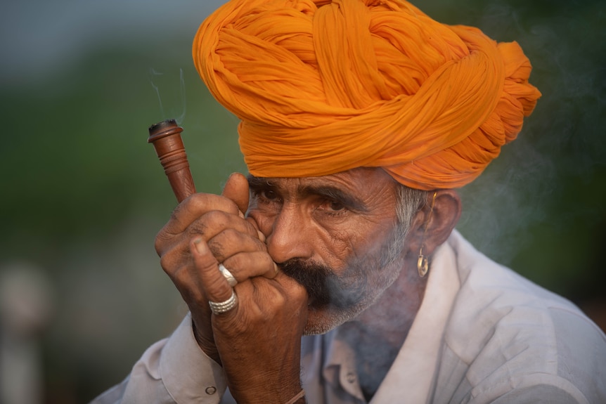 A man in an orange turban smokes a pipe.