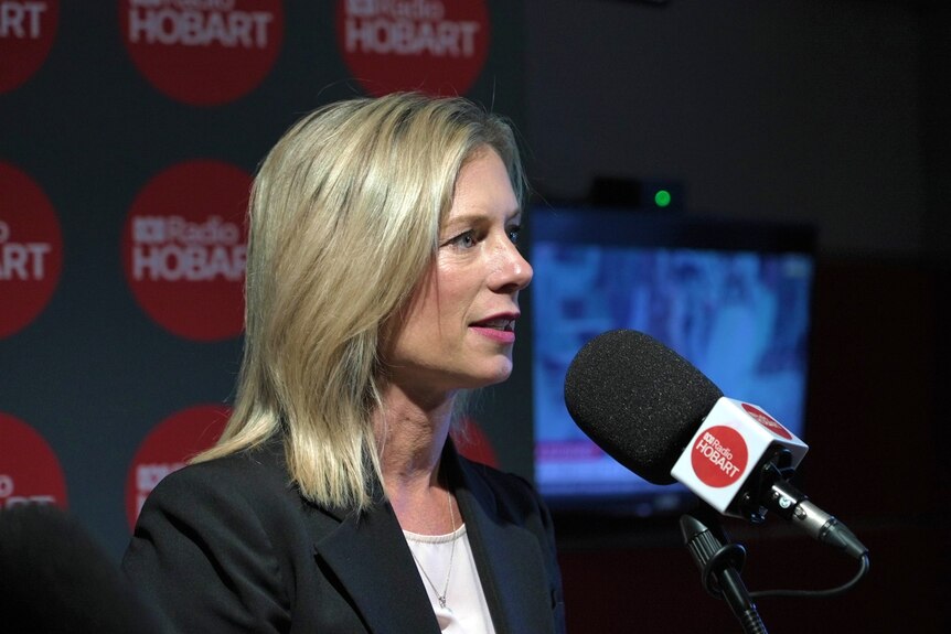 Rebecca White has shoulder-length blonde hair and is speaking into a radio microphone.