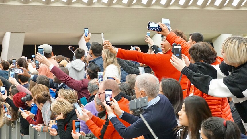 A large group of people hold up dozens of mobile phones to take a picture
