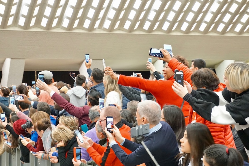 A large group of people hold up dozens of mobile phones to take a picture