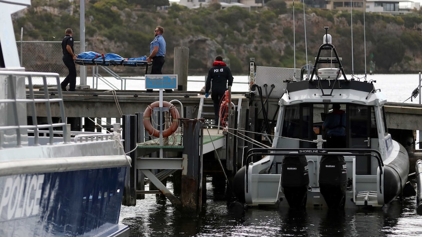 Police carry a plastic covered body strapped to a stretcher across a jetty in Fremantle.