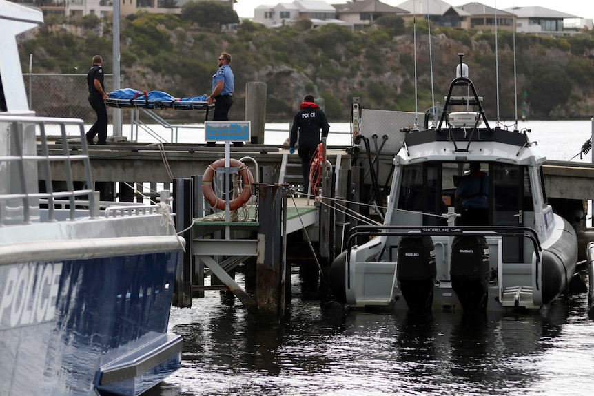 Police carry a plastic covered body strapped to a stretcher across a jetty in Fremantle.