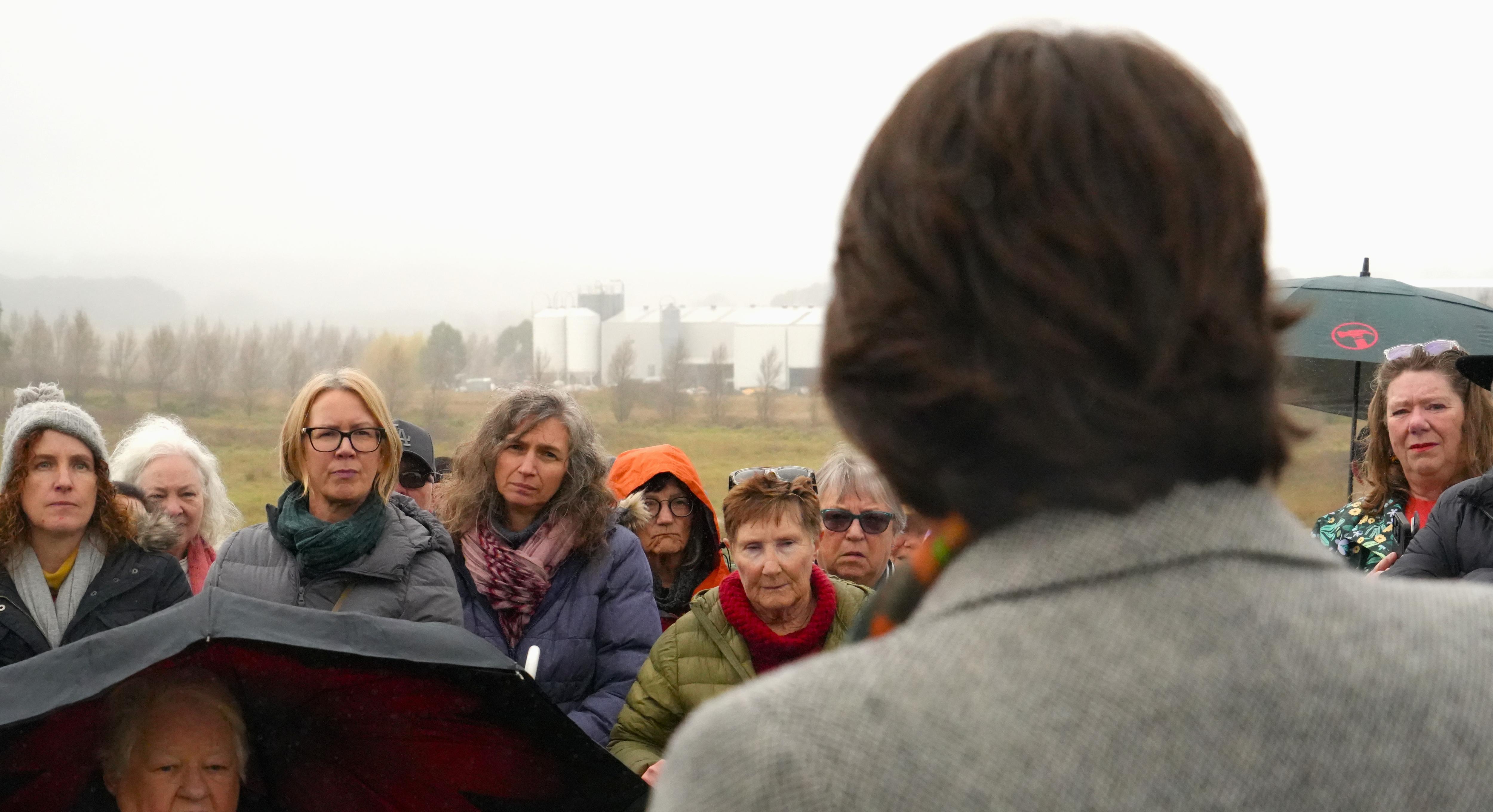 person in foreground speaks to gatehred people in wet weather gear