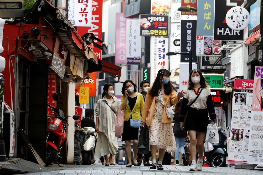 A group of young Korean women walk through a busy street in a shopping district.