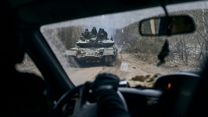 A Ukrainian tank with soldiers is seen through a car window.