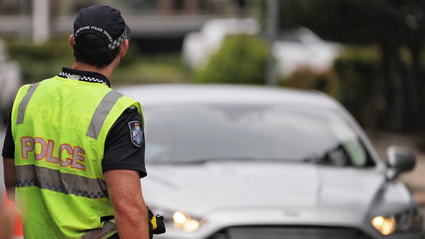 Queensland police officer in high-vis directs a car driving on road near a border checkpoint at Coolangatta.