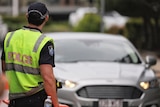 Queensland police officer in high-vis directs a car driving on road near a border checkpoint at Coolangatta.