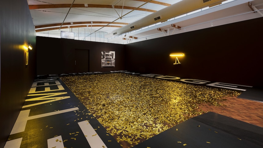 Large gallery space with a rectangle in the centre filled with gold confetti, with sculptural work around the outside