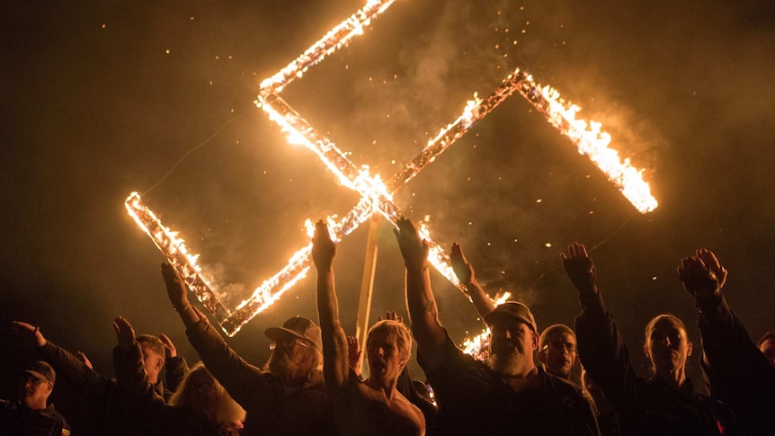 A swastika burns as a group of men give the Hitler salute