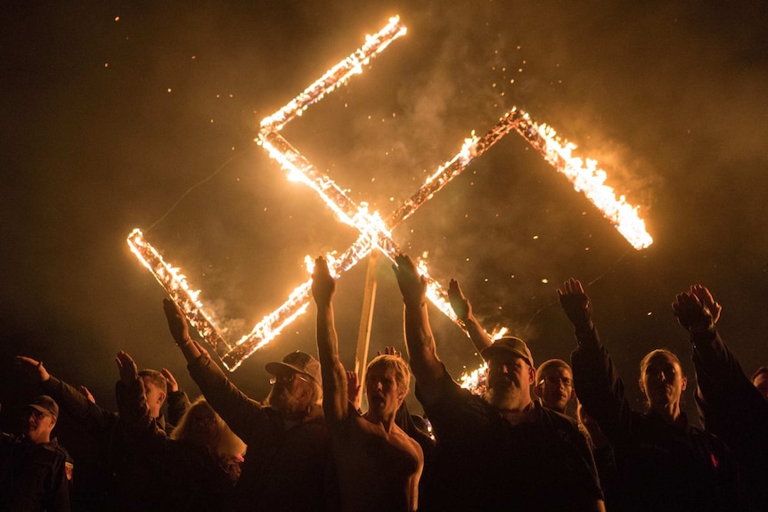 A swastika burns as a group of men give the Hitler salute