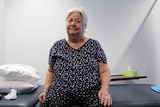 A photo of 83-year-old woman Eileen Farrar sitting on a bed in a physiotherapist's office.
