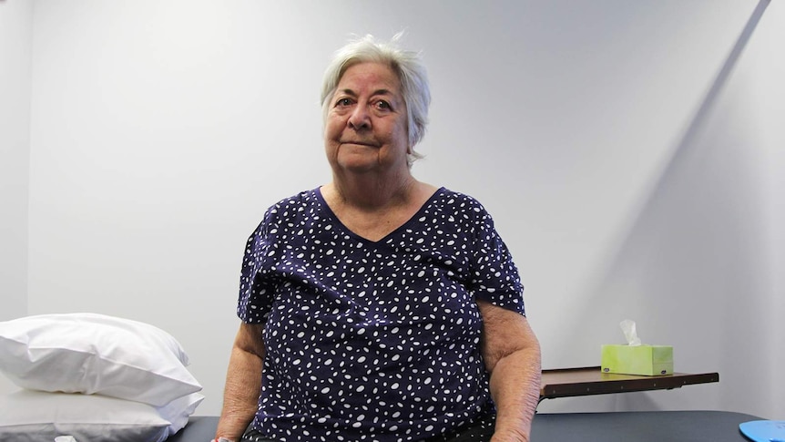 A photo of 83-year-old woman Eileen Farrar sitting on a bed in a physiotherapist's office.