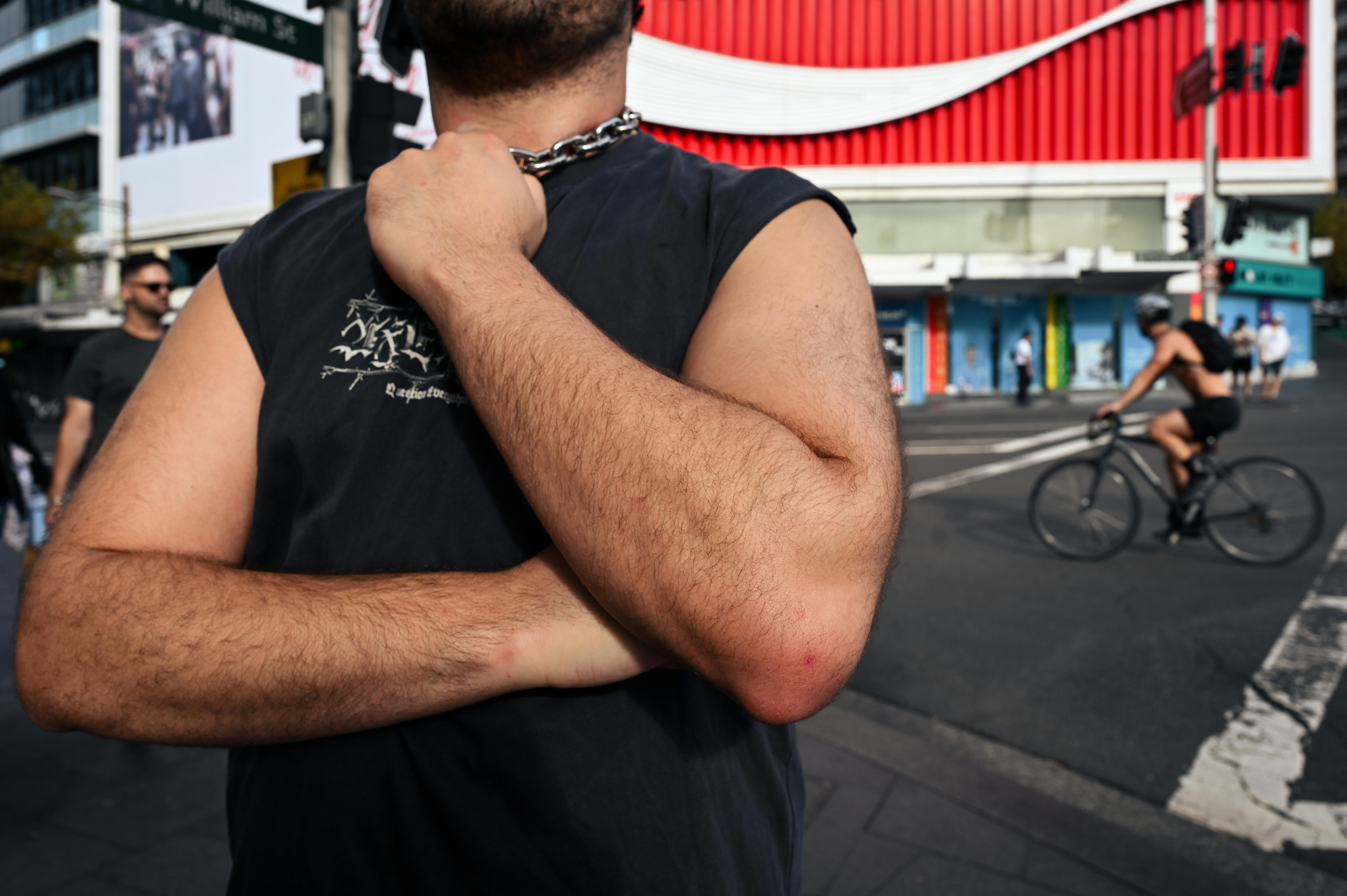 A man with hairy arms and fair skin in a black singlet grabs a chain around his neck.