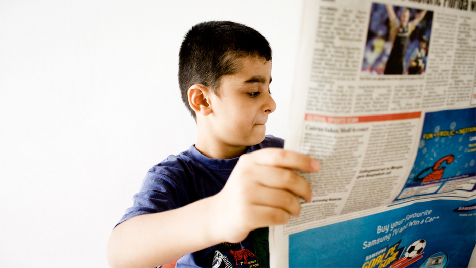 A young boy reads a newspaper.