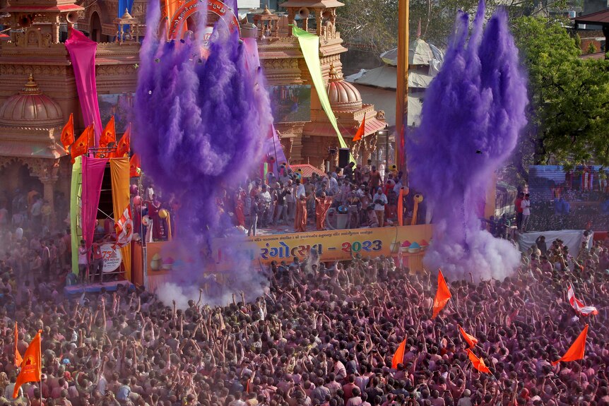 A festival crowd is pictured with two large blasts of purple powder in the sky.