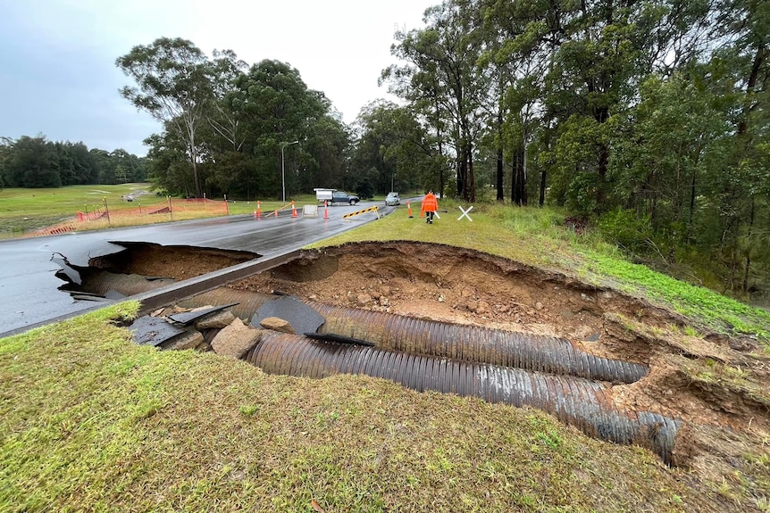 Large sink hole across road and adjacent grass exposing pipes