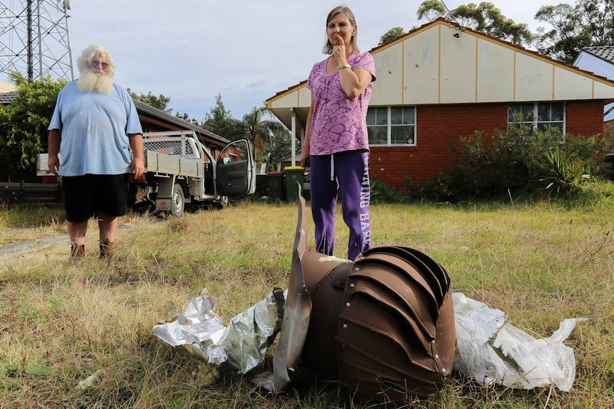People look at a large metallic object in the front yard of a house.