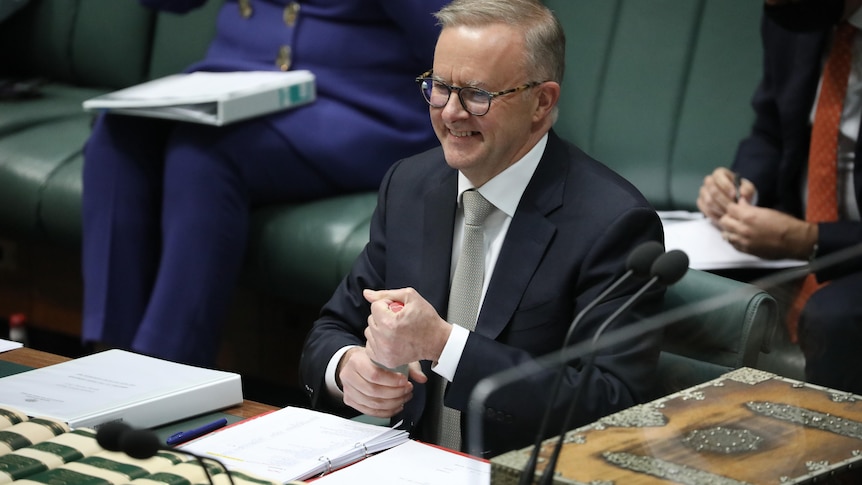 Albanese smiles as he wraps two hands around a bottle to open the lid