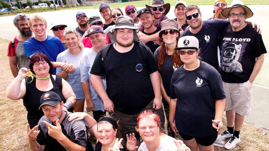 A large group of people pose outdoors at a netball court where they have just finished exercising.