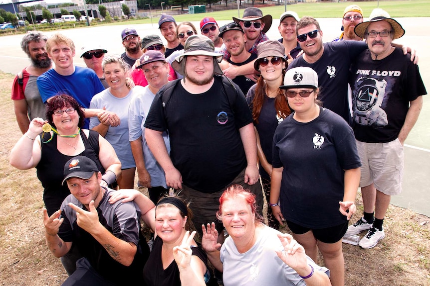 A large group of people pose outdoors at a netball court where they have just finished exercising.