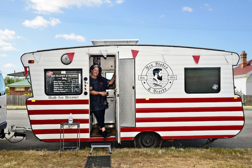 A woman stands in the doorway of a retro caravan, painted with red and white stripes. 