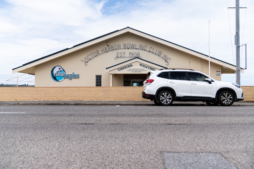 A wide shot of a the front of a bowling club with a white SUV parked in front