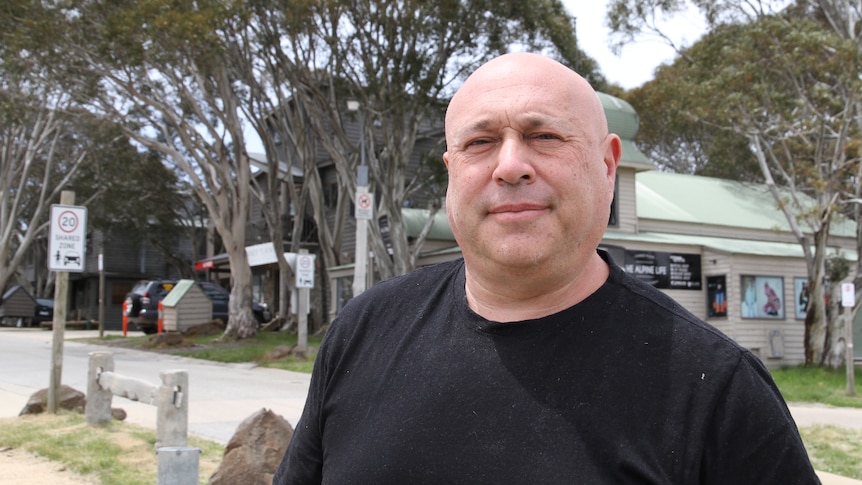 Steve Belli looking at the camera in the middle of Dinner Plain with building and trees in the background.