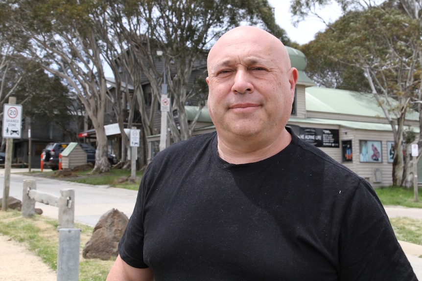 Steve Belli looking at the camera in the middle of Dinner Plain with building and trees in the background.