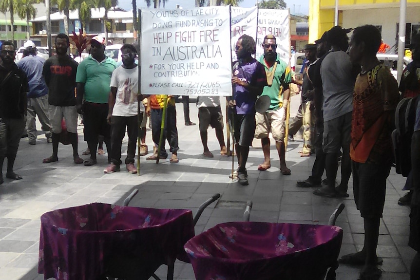 Young PNG nationals push wheelbarrow collecting cash donations and wave placards in support of Australian bushfire victims