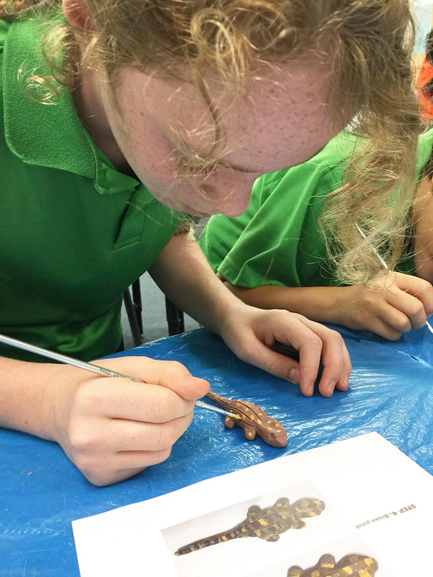 A girl from Bonython Primary School paints a clay earless dragon model.