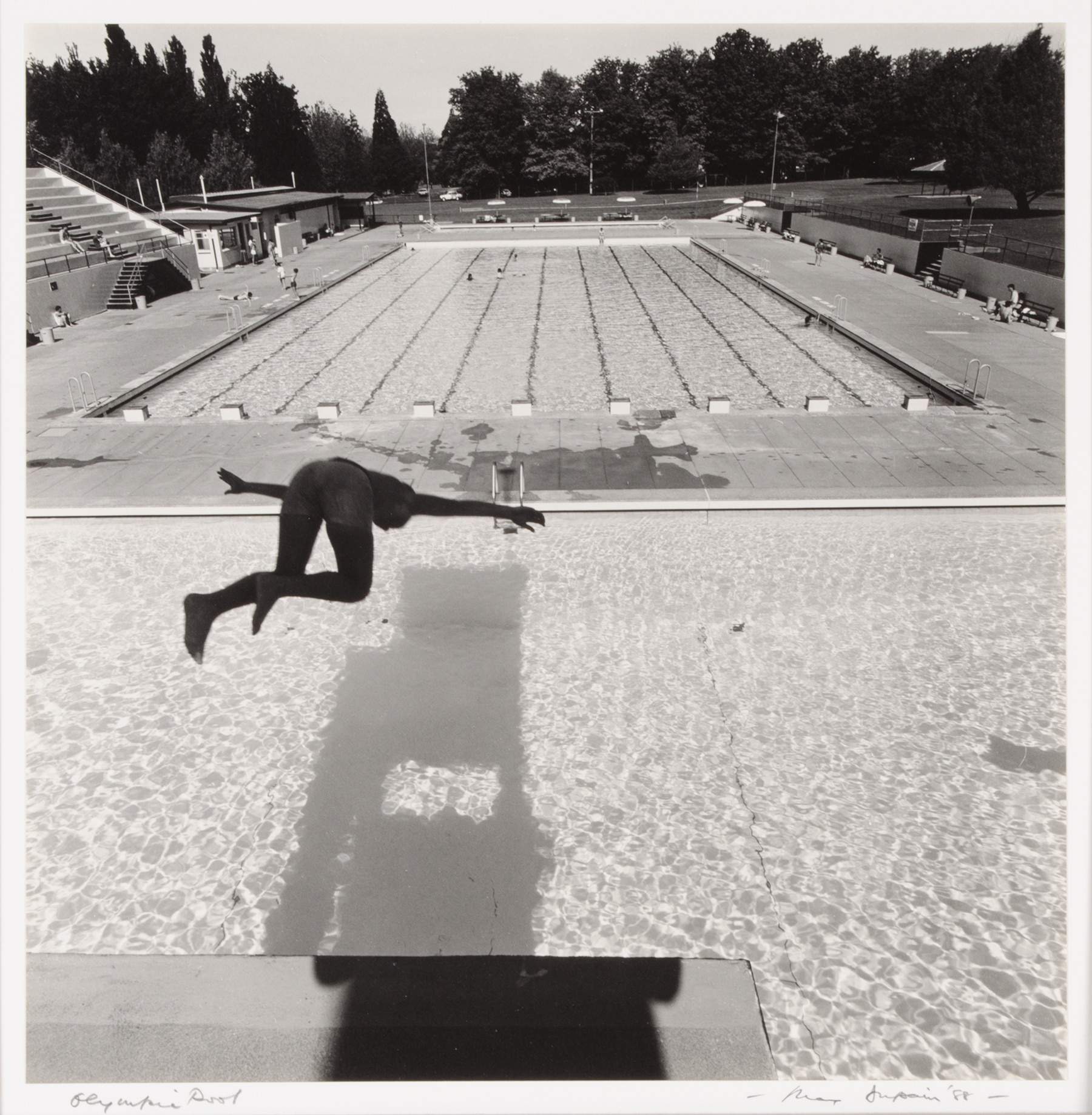 Uma fotografia em preto e branco de uma figura sombria saltando de uma torre de mergulho em uma piscina, além de uma piscina olímpica.