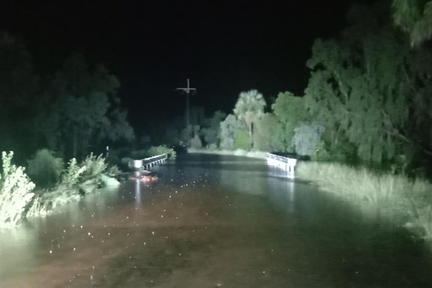 Water across a road at night in the bush, lit by headlights.