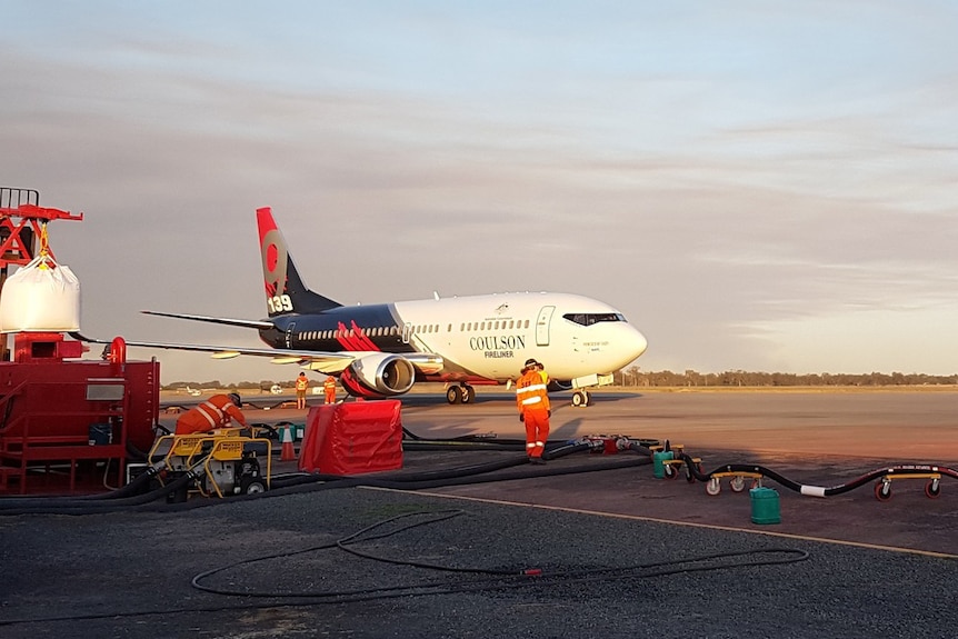 A Boeing 737 Fireliner large air tanker on the tarmac at Busselton airport, with refuelling gear and crew in the foreground.