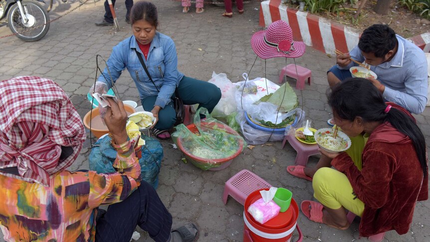 Women sit on small stools and eat soup noodles.