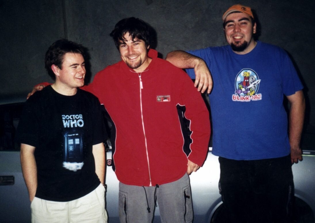 A male teenager in a Doctor Who T-shirt stands next to a male teen in a red jacket, and a third, wearing a blue Blink-182 