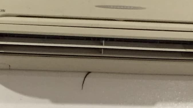 A photo of a snake's tail poking out from behind an air-conditioner.