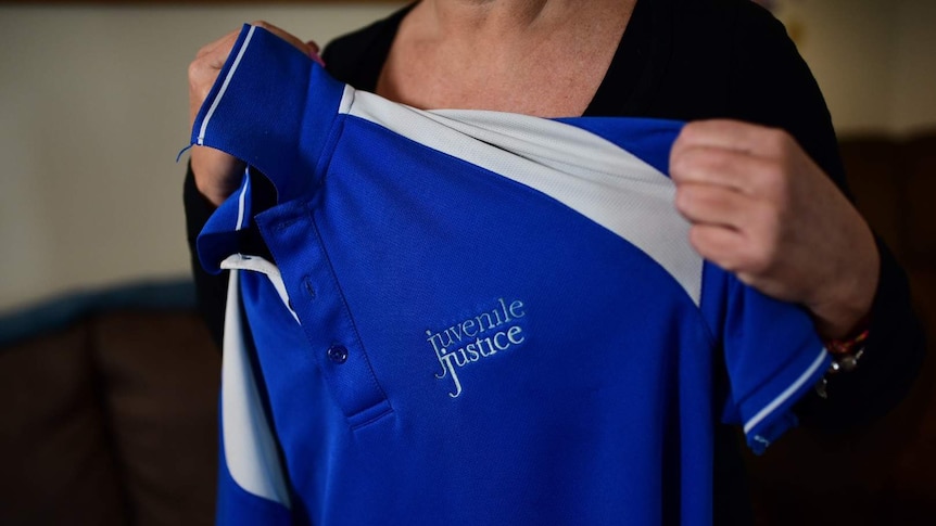 A woman holds up a uniform that says 'Juvenile Justice'.