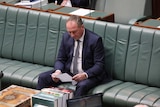Barnaby Joyce sits alone on the Government front bench in the House of Representatives. He is reading a piece of paper